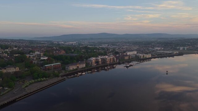 Aerial view of the River Foyle waterfront at sunset with historic buildings and calm water reflecting the sky in Derry, Northern Ireland, United Kingdom.