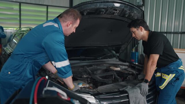 Two mechanics examine a car engine together. They lean over open hood