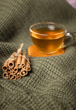 A knitted throw with a cup of green tea and cinnamon sticks on an autumn day.