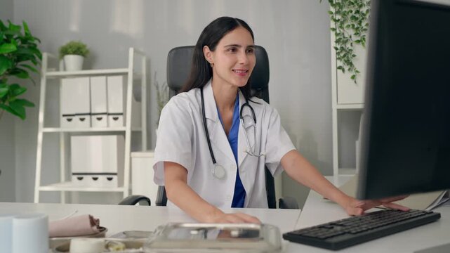 Female doctor typing on computer while reviewing patient record in hospital. 