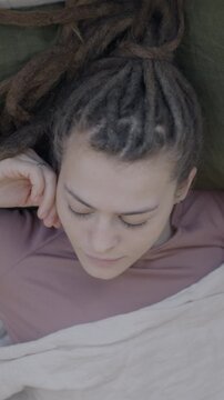 Top view of young woman with dreadlocks sleeping in bed on pillow under blanket moving in sleep enjoying rest. People and bedtime concept.