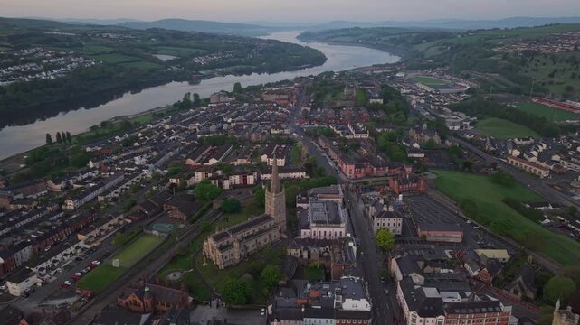 Aerial view of the historic city of Londonderry with the River Foyle flowing through the urban landscape, featuring stone buildings and green spaces in Londonderry, United Kingdom.