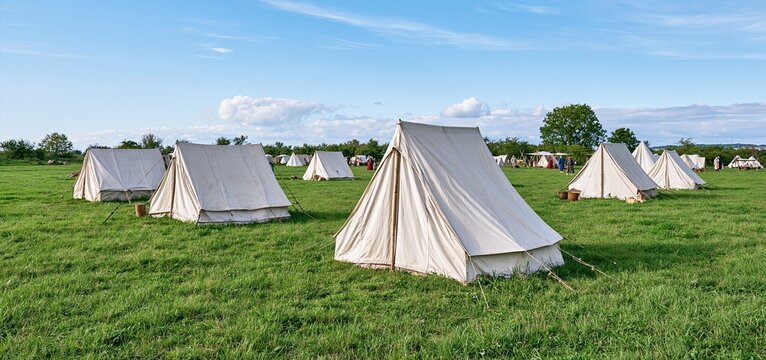 Canvas tents set up in a medieval reenactment camp with participants dressed in period clothing.
