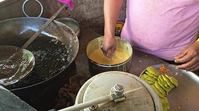 Action Close Up of Street Vendor Alternating Both Hands to Coat Spiced Potato Mix in Yellow Gram Flour Batter and Transfer to Hot Frying Oil Wok for Crisp Vada Pav Preparation at Open Food Stall