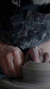 Close-up of skilled craftsman shaping ceramic pot from clay working with throwing wheel in studio. Occupation and pottery equipment concept.