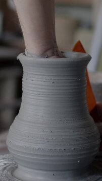 Close-up of artist creating beautiful ceramic vase with professional tools and spinning wheel in workshop. Traditional arts and small business activity concept.
