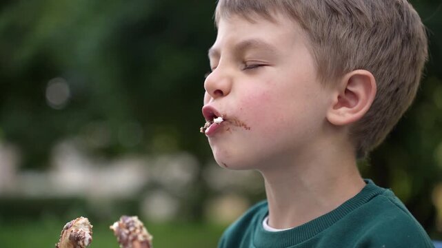 Young boy eating a traditional pretzel while sitting on a park bench, illustrating childhood, outdoor leisure and everyday moments.