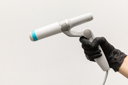 Close up hand in black glove holds handle of device for non-surgical ultrasound SMAS lifting procedure, white background. Figure shaping, body correction, fat burning, weight loss. Copy space