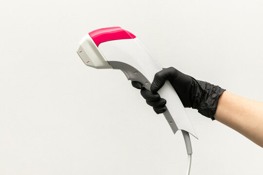 Close up hand in black glove holds handle of device for non-surgical ultrasound SMAS lifting procedure, white background. Figure shaping, body correction, fat burning, weight loss. Copy space