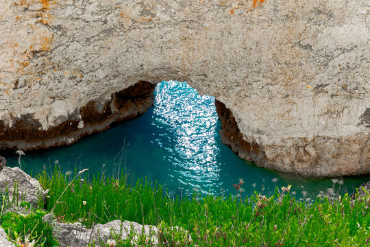 Natural rock archway frames tranquil turquoise water bay with lush green coastal vegetation