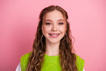 Obraz premium Young smiling female student with braces wearing a bright green vest style sweater against pink background showcasing happiness school fashion lifestyle and casual youth vibe