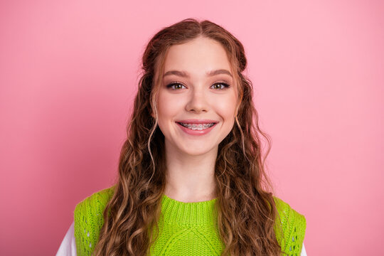 Young smiling female student with braces wearing a bright green vest style sweater against pink background showcasing happiness school fashion lifestyle and casual youth vibe