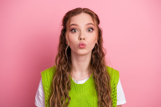 Young female teen girl with pink background wearing a bright green vest making a playful kissy face