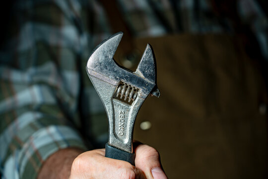 Closeup of hand holding heavy adjustable wrench. Mechanic or carpenter hand gripping vintage steel spanner repair worker with industrial hand tool wearing protective apron background