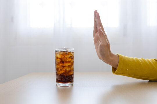 Sugar reduction concept, person refusing glass of sugary soda with ice on table at home, healthy choice, nutrition, wellness, diet, prevention, lifestyle.