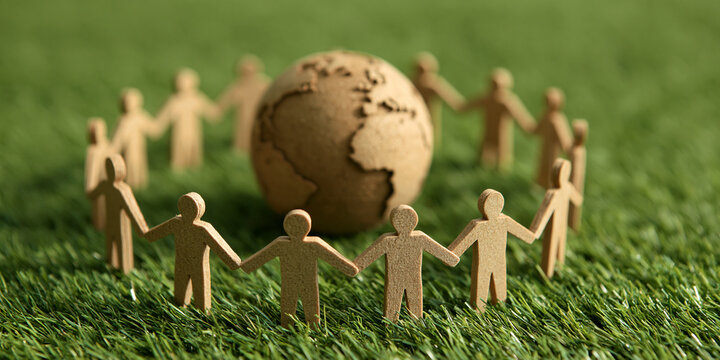 A circle of paper people holding hands around a globe on a lush green grassy surface, symbolizing global unity and environmental connection