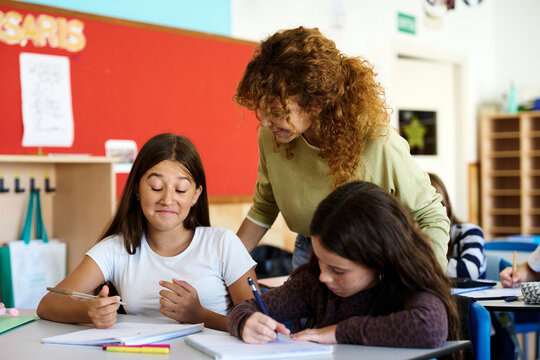 Teacher helping schoolgirls studying in classroom
