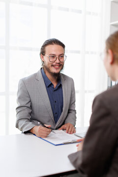 Happy male candidate smiling, discussing career opportunities and personal qualifications during a job interview, signing an employment application in a modern office