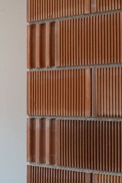 Textured terracotta brick wall with alternating smooth and ridged courses, vertical grooves, mortar joints, warm earthy tones, and repeating architectural pattern