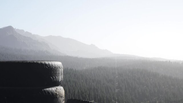 Old tires are stacked in the foreground with a view of mountains and trees in the background. The scene shows a clear sky and distant hills at dusk or dawn.