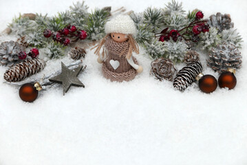 Fototapeta premium Christmas decoration featuring a small doll, pine cones, twigs, red berries, and Christmas baubles on snow, with copy space.