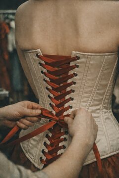 Dresser hands tighten satin ribbon corset ties on actress before show