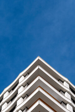 Apartment building corner rises into blue sky where balconies create symmetrical residential perspective and repeating geometry across the modern facade