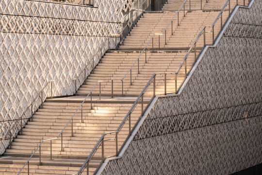 Outdoor staircase climbs between patterned walls with metal railings where perspective and repetition create geometric rhythm across the architectural space
