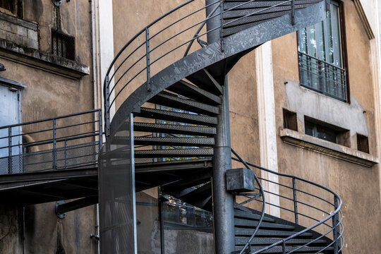 Metal spiral staircase wraps around an aged urban building facade where circular steps and railings create repeating geometry across the exterior architecture