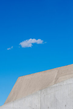 Minimal concrete roofline crosses bright blue sky with a small cloud where architecture and geometry create generous copy space above the building edge