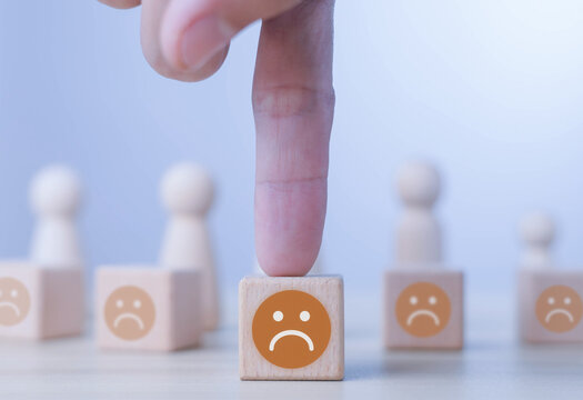Customer dissatisfaction concept showing one hand selecting a sad wooden block, symbolizing negative feedback, poor service, unhappy customers, emotional response, evaluation, and business reputation.