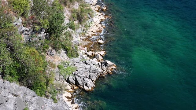 Clear turquoise sea water along a rocky Mediterranean coastline with green coastal vegetation on a sunny summer day.