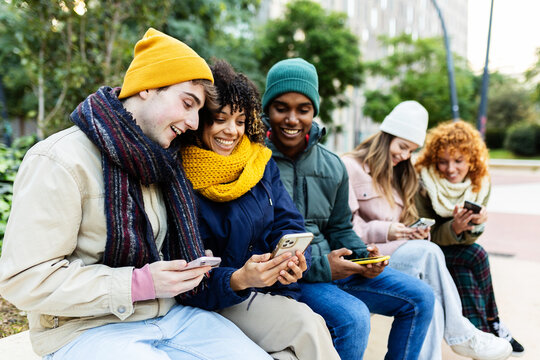 Happy young students using smartphones at city street on winter. Social media and technology lifestyle concept