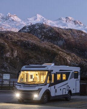View of a modern motorhome parked near Lake Enol with snow-capped mountains in the background during twilight in Asturias, Asturias, Spain.