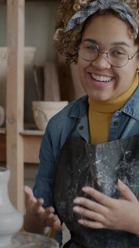 Portrait of creative influencer recording video about pottery in workshop talking and making pot. Joyful vlogger having fun with clay and speaking then waving hand.