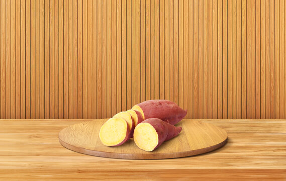 Raw sweet potato on round wooden board with wooden background.