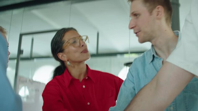 Coworkers celebrate team success in a bright office with a hands-in huddle, cheering and clapping together. Business teamwork, collaboration, unity, motivation, and positive workplace culture are clea