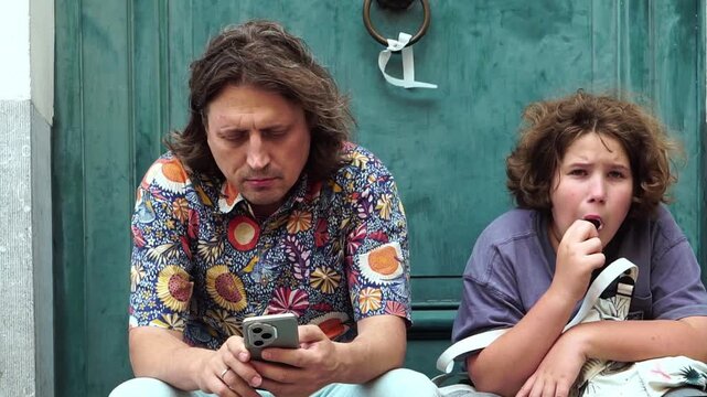 Father checking a smartphone beside a son eating ice cream