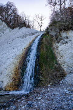 View of a waterfall cascading down the white chalk cliffs of Rugen with a rocky beach and bare trees in Mecklenburg-Vorpommern, Germany.