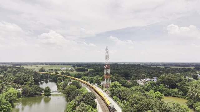 Drone footage shows a cargo train arriving at historic Poradah Junction in Kushtia, Bangladesh, moving along railway tracks between station platforms amid lush greenery, ponds, homes, and farmland.