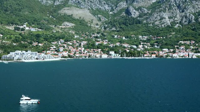 White yacht on blue water near a seaside town with mountains in the background. Scenic Adriatic coast travel destination on a sunny day.