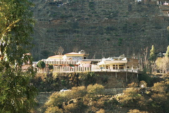 View of houses situated on a terraced hillside along Shangla Road with rocky slopes and surrounding trees in Martung, Khyber Pakhtunkhwa, Pakistan.