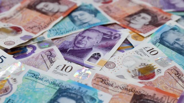 Heap of British pound banknotes with portraits of Queen Elizabeth II and King Charles III.
