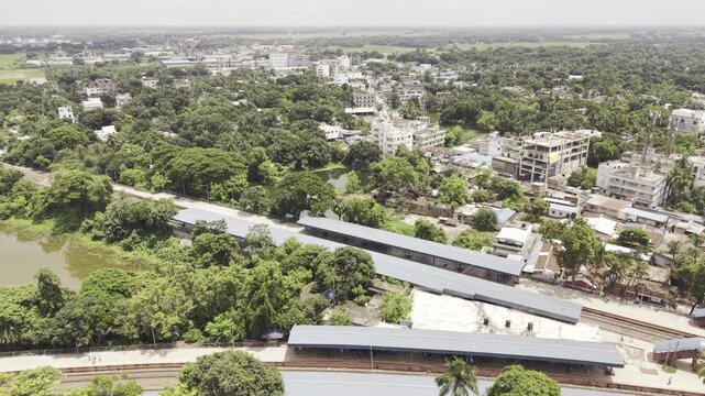 Forward-moving aerial drone footage of Poradaha Junction Railway Station in Bangladesh, showing railway platforms, multiple tracks, station buildings, surrounding greenery, and the nearby landscape.