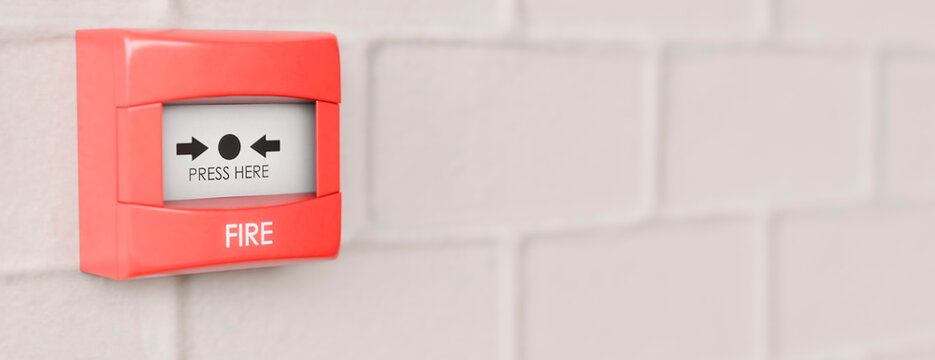 Red fire alarm pull station mounted on a white brick wall for safety