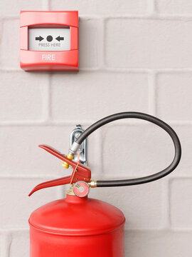 Red fire extinguisher and alarm mounted on a white brick wall for safety
