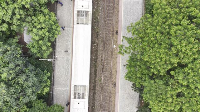 Aerial drone footage of a railway station in Bangladesh, showing multiple tracks, long platform roofs, station areas, pedestrian paths, and dense green trees surrounding the railway.