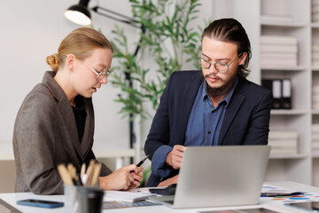 Fototapeta premium Business people collaborating on a project, analyzing data and discussing financial charts in an modern office setting, using a laptop for digital analysis and strategic planning