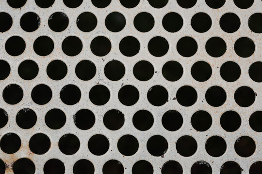Close-up of a perforated metal bench backrest showing a repeating circular hole pattern and contrasting geometric texture.