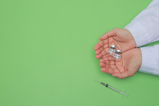 Professional focused scientist hand holding peptide vial and syringe during biotechnology research with hopeful care on plain green background